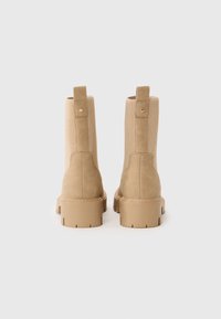 Bottes beiges à la cheville avec une tige en daim doux, des côtés élastiques nervurés et une semelle en caoutchouc épaisse. Comprend une languette au dos et des accents de couture.