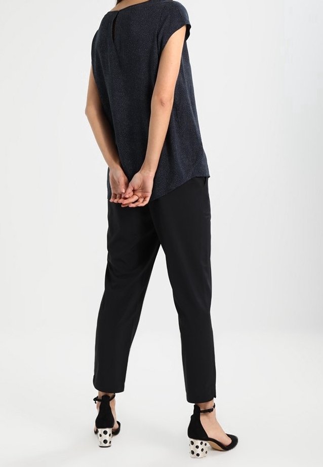 Černý top s krátkým rukávem a texturovaným povrchem, spárovaný s černými zúženými kalhotami a černými botami s puntíkovými akcenty.