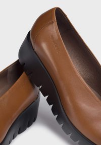 Zapatos de cuero marrón con un diseño elegante, que cuentan con una suela negra de patrón zigzag y un acabado suave en la parte superior.