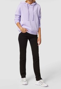 Sudadera con capucha en color lavanda, con bolsillo tipo canguro y cordones, combinada con jeans negros ajustados y zapatillas blancas. Conjunto sencillo y casual.