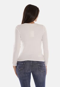 Maglione lungo grigio chiaro a maniche lunghe con collo rotondo, texture liscia e design aderente, abbinato a jeans in denim blu scuro con tasche posteriori.
