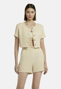 Cremfarbener, texturierten Zweiteiler bestehend aus einer kurz geschnittenen Jacke mit Knöpfen und passenden, hoch taillierten Shorts, die über ein gewebtes Muster und ausgefranste Kanten verfügen.