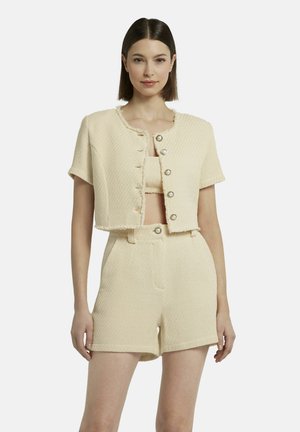 Ensemble deux pièces de couleur crème avec une veste cropped à boutons et un short taille haute coordonné, présentant un motif tissé et des bords effilochés.