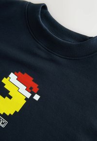 Felpa blu navy con un design pixelato arricchito da accenti gialli, rossi e bianchi sul davanti, colletto a coste e trama morbida.