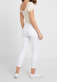 Białe dopasowane jeansy z wysokim stanem i skróconą długością, zestawione z górą z paskami i bufkami w jasnych kolorach.