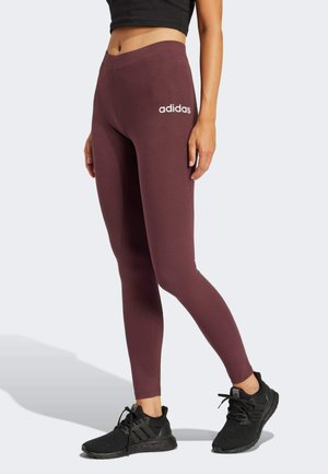 Leggings bordeaux en tissu extensible, avec une texture lisse et un logo Adidas blanc sur la cuisse gauche. Assortis à des chaussures de sport noires.