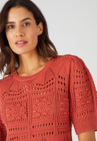 Maglione corto a maniche corte color corallo, con motivi a rete, colletto tondo e finitura testurizzata.