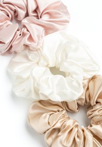 Set di tre scrunchies in satin di colore rosa chiaro, bianco e beige. Ognuno presenta una texture arricciata e un elastico per una presa sicura.