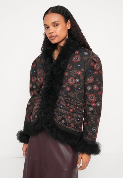 Črna vezenina jakna z rožnatimi vzorci v rdeči, modri in rjavi barvi, z puhastimi črnimi ovratnikom in manšetami, v kombinaciji z burgundijsko usnjeno krilom.