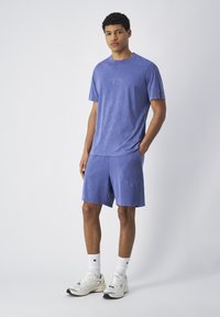 Lavendel katoenen T-shirt en short set met een ontspannen pasvorm, voorzien van een logo op de borst en het linkerbeen. Gemaakt met witte Champion sokken en sneakers.