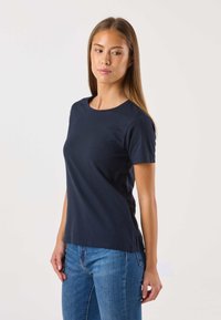 Laivastonsininen puuvillainen t-paita, jossa on klassinen pyöreä pääntie, lyhyet hihat ja suora helma, yhdistetty sinisiin farkkuihin.