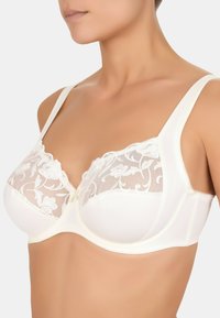 Witte beha met doorschijnende geborduurde kantcups, ondersteuning door beugels en verstelbare bandjes. Glad stof en bloemenpatroon op kant.