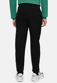 Svarta sweatpants med en tapered bendesign, elastisk midja och sidofickor, kombinerade med vita och gråa sportskor.