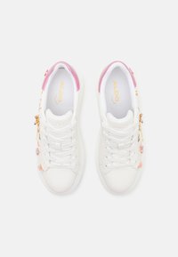 Baskets blanches en cuir texturé, accents roses sur le talon et décorations en forme de charms sur le côté featuring des fleurs et des formes géométriques.