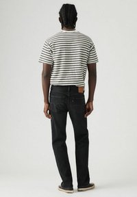 Gestreept t-shirt met korte mouwen in zwart en wit, gecombineerd met zwarte spijkerbroek. Kenmerkend ontwerp van de achterzak en een patch op de broek.