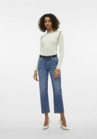 Top bianco a maniche lunghe con righe, rifinito con piping nero, abbinato a jeans dritti celesti, cintura nera e tacchi beige.