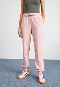 Pink fleece sweatpants with an elastic waistband, drawstring, and cuffed ankles. Features a small white logo on the left side.