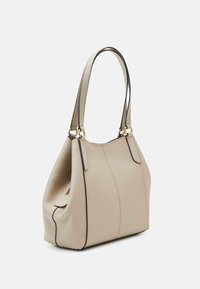 Beige leren handtas met gestructureerde vorm, twee schouderbanden bevestigd met gouden ringen, en zichtbare stikdetails.