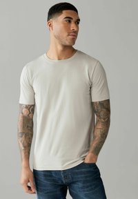 Maglietta grigia chiaro a maniche corte con scollo rotondo, abbinata a jeans blu scuro. Presenta una texture liscia e una linea aderente.