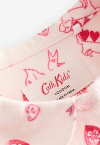 Różowy materiał z czerwonymi wzorami zwierząt i serc, z wszytą metką odzieżową Cath Kids London.