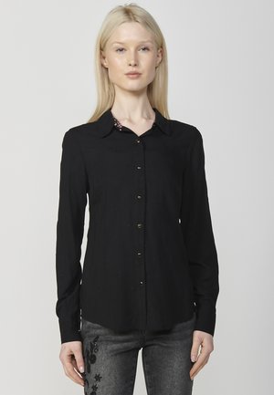 Camicia nera a maniche lunghe con colletto, caratterizzata da sottili pattern testurizzati e bottoni dorati lungo la parte anteriore.
