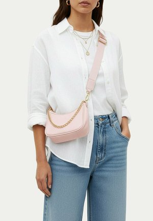 Frau trägt weißes Hemd und Jeans mit einer hellrosa Umhängetasche, die eine goldene Kette und einen verstellbaren Riemen hat.