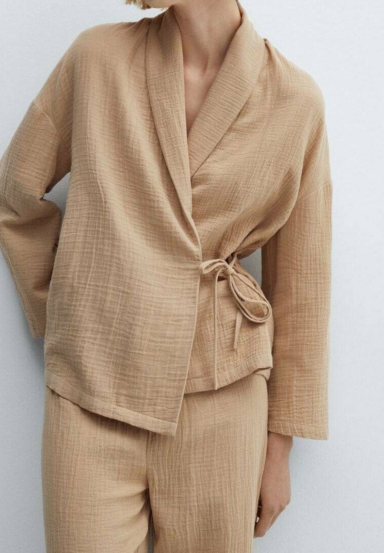 Beige, teksturoitu kietaisupaita shawl-kauluksella ja sivusolmulla. Rentoutunut istuvuus ja pitkät hihat, yhdistetty samansävyisiin housuihin.