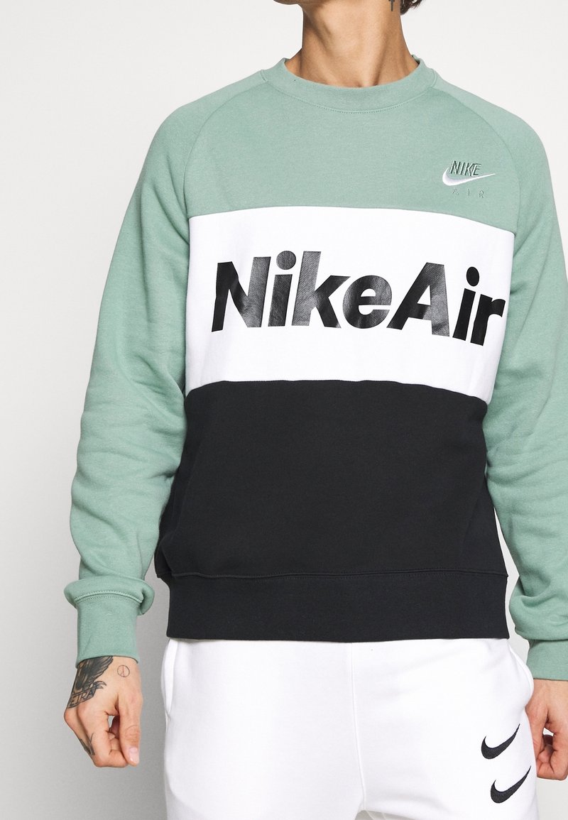 Grön, vit och svart sweatshirt med "Nike Air" i fet svart text. Tillverkad av mjukt tyg med ribbade ärmmuddar och rundad halsringning.
