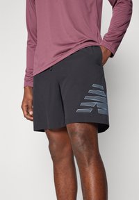 Sorte svøm shorts med et lyseblåt linært grafisk mønster på siden, lavet af et letvægtsmateriale. Designet har en afslappet pasform.