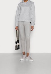 Grå hoodie med dragsko i huva, ljusgrå ripped skinny jeans, blekrosa sneakers med vita sulor, och en liten svart crossbody-väska.