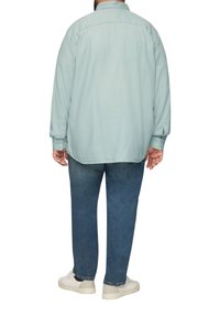 Lichtblauw shirt met lange mouwen en een rugpand, gecombineerd met donkerblauwe jeans en witte sneakers. Gladde textuur, ontspannen pasvorm.
