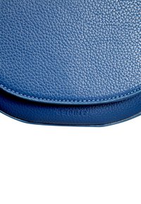 Blå läder crossbody-väska med en texturerad yta, rundad form och präglad logotyp. Har kontrasterande sömmar längs kanten.