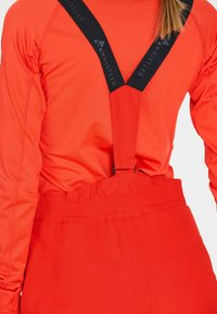 Rode thermische longsleeve top met zwarte verstelbare bandjes met een logo, gecombineerd met rode hoge taille broek met elastische tailleband.