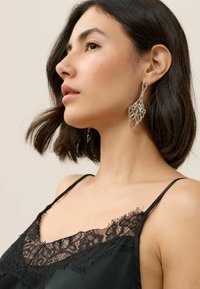 Camisón de satén negro con encaje, que presenta delicados patrones florales y tirantes ajustables, acompañado de un gran y elaborado pendiente de plata.