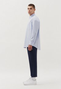 Camicia azzurra a righe con bottoni e maniche lunghe, indossata con pantaloni scuri e sneakers bianche. Presenta una tasca sul petto e una vestibilità comoda.