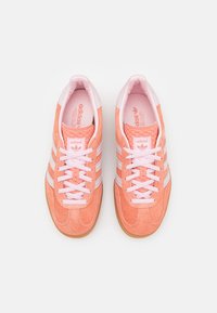 Sneakers in camoscio arancione con accenti rosa, dotati di tre strisce bianche e design con lacci. Punta arrotondata e dettagli testurizzati sulla linguetta.