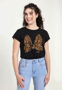 Schwarzes T-Shirt mit einem großen Leopardenmuster-Schleifendesign in Brauntönen. Kurze Ärmel, runder Ausschnitt, kombiniert mit hellblauen Jeans.