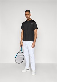 Čierne tričko s krátkym rukávom športového strihu s logom, doplnené bielymi tenisovými nohavicami. Postava drží čiernu tenisovú raketu s modrými akcentmi.