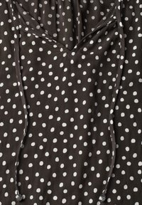 Black fabric with irregular white polka dots and a V-shaped neckline with attached narrow ties hanging down.
