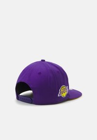 Gorra de béisbol morada con corona estructurada, visera plana, correa ajustable y logo bordado de los Los Angeles Lakers en el lateral.