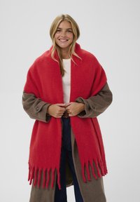 Red and brown wool blend oversized shawl with fringed edges. The shawl has a soft texture and a relaxed design, wrapped around the wearer.