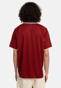 Mørkerød polo-shirt med krave, der har hvide detaljer på kraven og ærmerne. Glat, let materiale med en afslappet pasform.