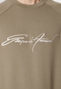 Olivgrön sweatshirt med rund halsringning, med vit broderad signaturtext. Mjuk, slät tygkänsla och raglanärmar.