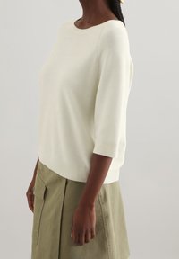 Pull en tricot crème clair avec des manches trois-quarts, encolure et ourlet côtelés, associé à une jupe vert sauge avec une poche latérale.