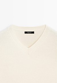 Maglione beige a V con una texture morbida, colletto a costine e dettagli di cucitura discreti. L'etichetta visibile all'interno del colletto reca la dicitura "Massimo Dutti."