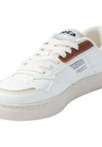 Hvite skinn-sneakers med en teksturert off-white såle, brune detaljer og svart merke på tungen; har perforeringer på tåen.