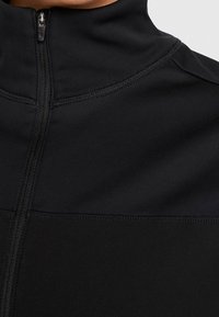 Sort atletikjakke med høj krave, udstyret med en central lynlås og flatlock-sømme, lavet af et glat, elastisk stof.