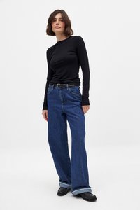 Svart långärmad topp, blå vida jeans med bälte. Jeansen har klassisk femfickdesign och uppvikt nederkant. Svarta skor fulländar outfiten.