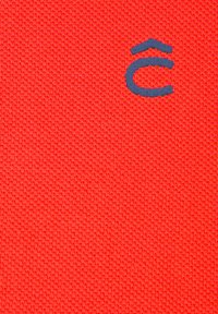 Czerwony, dziany materiał z niebieskim logo. Tekstura jest gładka, o drobnym splocie, podkreślająca intensywny kolor i graficzne detale.