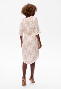 Kurzes Damenkleid in Hellrosa mit gewelltem Goldmuster, tailliert in der Taille. Glattes Material mit fließender Silhouette und mittellanger Säume.